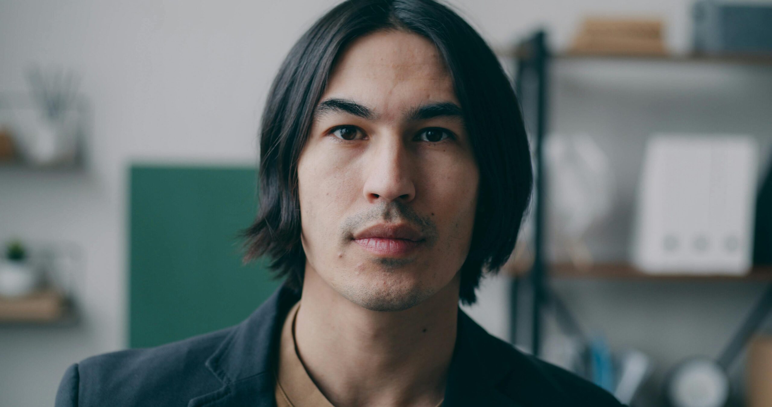 Portrait of a thoughtful adult man with long hair in an indoor setting.